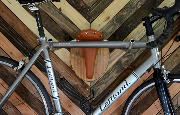 Wall mounted bike rack shaped like a longhorn, made with wood, leather seat, and handlebars – decorative indoor bicycle holder
