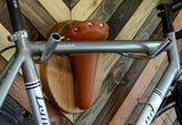 Wall mounted bike rack shaped like a longhorn, made with wood, leather seat, and handlebars – decorative indoor bicycle holder
