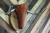 Wall mounted bike rack shaped like a longhorn, made with wood, leather seat, and handlebars – decorative indoor bicycle holder